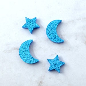 Puede incluir: Primer plano de una moneda de un céntimo con el año 2006 en ella, rodeada de cuatro formas de espuma azul con purpurina: dos medias lunas y dos estrellas de cinco puntas.