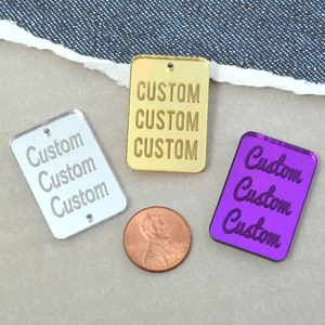 May include: Three rectangular acrylic tags with the word "Custom" written on them. The tags are silver, gold, and purple.
