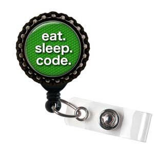 Könnte beinhalten: Ein schwarzer und grüner ausziehbarer Ausweishalter mit einem runden Metallanhänger, auf dem "eat. sleep. code." steht.