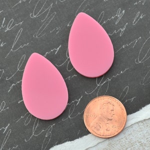 Könnte beinhalten: Zwei rosafarbene, tropfenförmige Acrylrohlinge, etwa so groß wie ein 1-Cent-Stück.