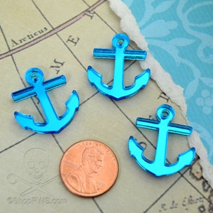 Può includere: Tre ciondoli a forma di ancora in acrilico blu brillante. I ciondoli sono di un vibrante colore turchese e sono posizionati su uno sfondo di mappa vintage. Viene inclusa una moneta da un centesimo come riferimento delle dimensioni. Le ancore sono a tema nautico.