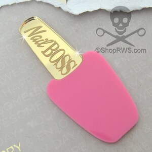 May include: Gold nail polish bottle charm with the words "Nail Boss" engraved on the cap. The bottle is pink.
