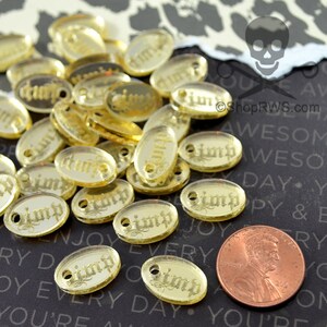 Puede incluir: Un mont&oacute;n de dijes ovalados de color dorado con la palabra "Pimp" escrita en ellos. Los dijes son aproximadamente del tama&ntilde;o de una moneda de un centavo de euro.