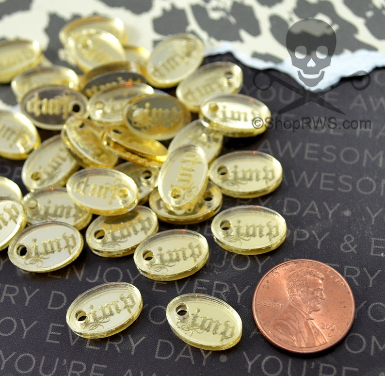 Puede incluir: Un mont&oacute;n de dijes ovalados de color dorado con la palabra "Pimp" escrita en ellos. Los dijes son aproximadamente del tama&ntilde;o de una moneda de un centavo de euro.