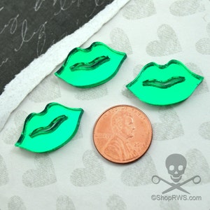 Peut inclure: Trois lèvres en acrylique vert, chacune avec une forme légèrement différente, sont disposées sur un fond blanc à motif de cœur. Une pièce de monnaie d'un cent est placée sous les lèvres pour comparaison de taille.