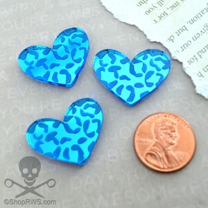 Op de afbeelding: Drie blauwe hartvormige acrylcharms met een luipaardprint. De charms zijn ongeveer zo groot als een Nederlandse cent.