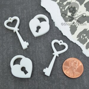 May include: Four white plastic heart-shaped lock and key charms. The charms are approximately the size of a US penny.