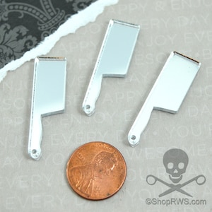 May include: Three silver mirror-like acrylic charms shaped like butcher knives. The charms are approximately the size of a UK penny.