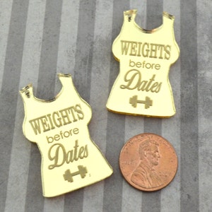 May include: Two gold mirror acrylic tank top shapes with the text "Weights before Dates" and a dumbbell symbol.