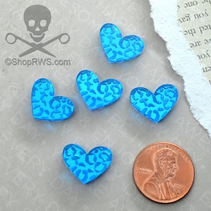 Op de afbeelding: Vijf blauwe hartvormige glazen kralen met een wit luipaardmotief. De kralen zijn ongeveer zo groot als een Nederlandse cent.