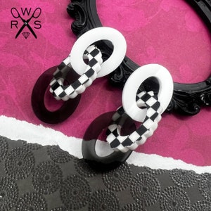 May include: A pair of black and white checkerboard patterned earrings with a white circle and a black circle on each earring.