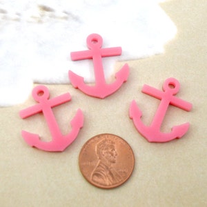 Può includere: Tre ciondoli a forma di ancora in plastica rosa. I ciondoli sono circa delle dimensioni di una moneta da un centesimo di euro.