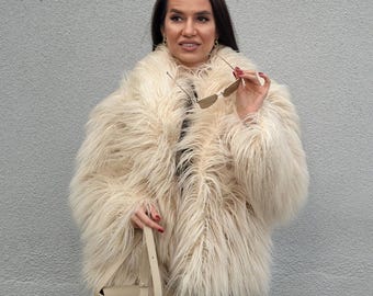 May include: A cream-colored faux fur coat with long, shaggy fur. The coat is paired with a small, beige shoulder bag and black pants. The person is holding sunglasses.