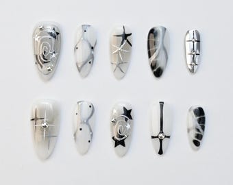 Uñas postizas góticas en negro y gris con forma de almendra, uñas grunge Y2K con estrellas cruzadas, uñas postizas alternativas cromadas con efecto mármol ahumado, juego de uñas moderno y artesanal.