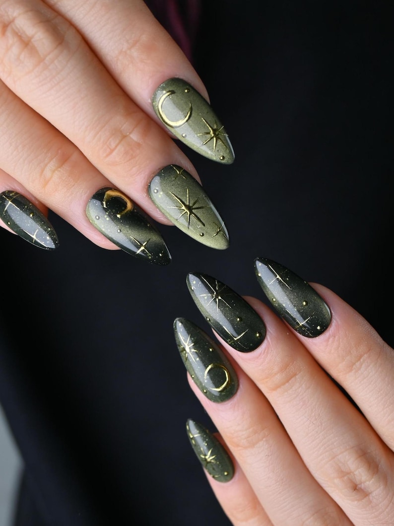 May include: Olive green almond-shaped nail design with gold celestial accents. Each nail features a gold crescent moon, stars, and small dots. The nails have a glossy finish, creating a stylish and unique look.