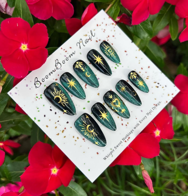 This nail set features a deep green base with intricate gold celestial designs, including stars, moons, and suns, creating a mystical and elegant look.