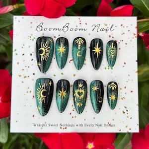 This nail set features a deep green base with intricate gold celestial designs, including stars, moons, and suns, creating a mystical and elegant look.