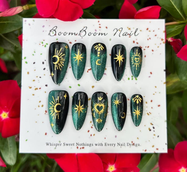 This nail set features a deep green base with intricate gold celestial designs, including stars, moons, and suns, creating a mystical and elegant look.
