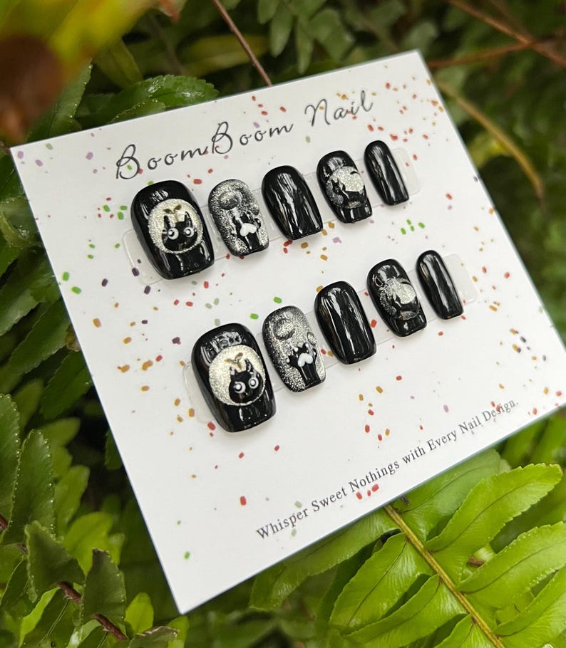 This nail set features a playful black base adorned with whimsical silver characters and patterns, adding a fun and mysterious vibe. Perfect for those who love unique, eye-catching designs with a touch of charm.