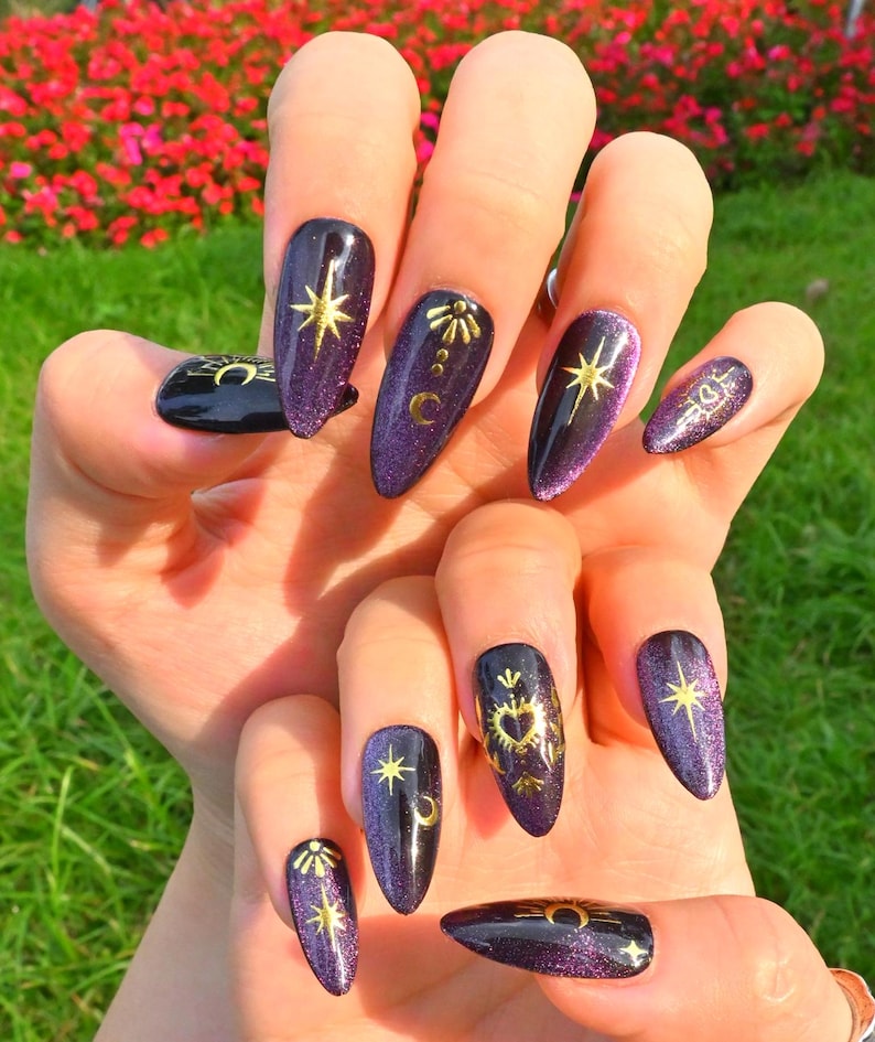 This nail design features a deep purple to black gradient base, adorned with gold celestial elements like the moon, sun, and stars, creating a luxurious and mystical vibe.