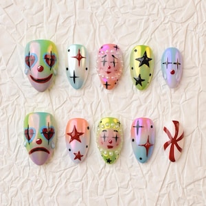 May include: A set of ten press-on nails featuring various designs including clown faces with heart-shaped eyes, black and red stars, white pearls, and a red and white swirl pattern. The nails have a glossy, iridescent finish in shades of pink, blue, and green.