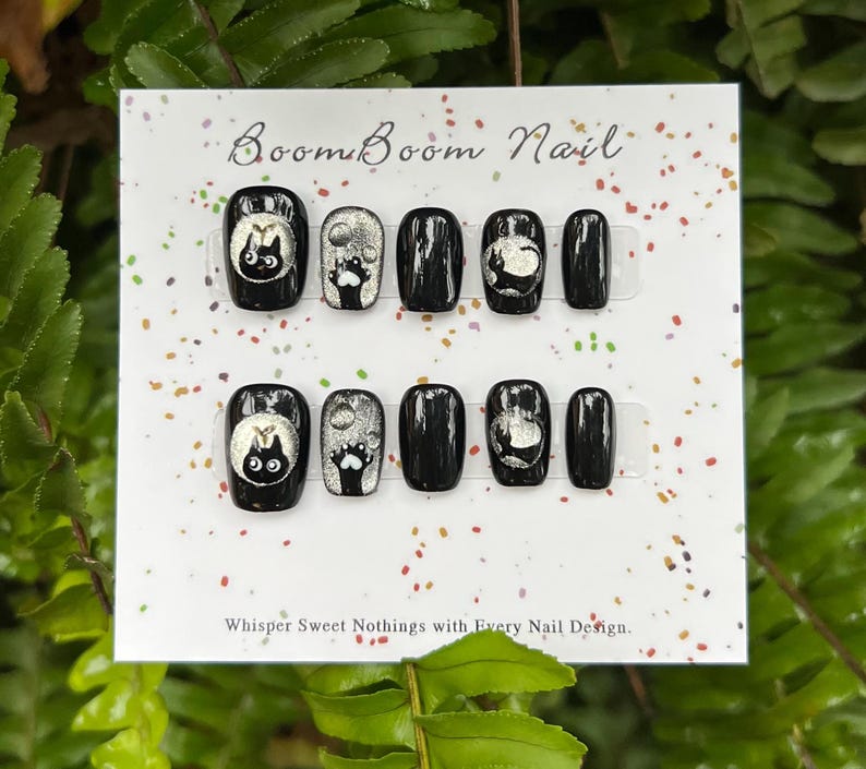 This nail set features a playful black base adorned with whimsical silver characters and patterns, adding a fun and mysterious vibe. Perfect for those who love unique, eye-catching designs with a touch of charm.