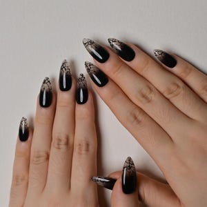 May include: Almond-shaped press-on nails featuring a gradient design that transitions from a solid black base at the tips to a translucent, cracked, or web-like pattern in shades of grey and white near the cuticles, creating a distinct contrast.