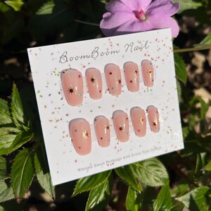 This nail set features a soft nude pink base adorned with delicate golden starbursts and colorful confetti details. Perfect for a playful yet elegant look that adds a touch of sparkle to any occasion.