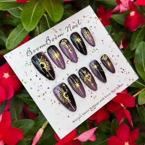 This nail design features a deep purple to black gradient base, adorned with gold celestial elements like the moon, sun, and stars, creating a luxurious and mystical vibe.