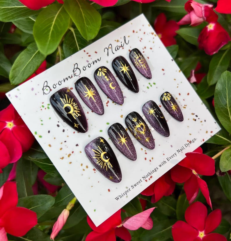 This nail design features a deep purple to black gradient base, adorned with gold celestial elements like the moon, sun, and stars, creating a luxurious and mystical vibe.