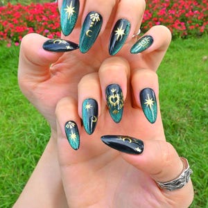 This nail set features a deep green base with intricate gold celestial designs, including stars, moons, and suns, creating a mystical and elegant look.