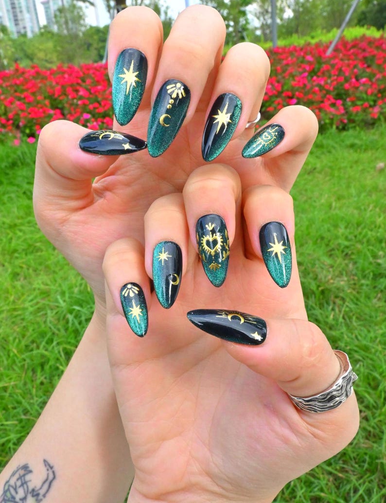This nail set features a deep green base with intricate gold celestial designs, including stars, moons, and suns, creating a mystical and elegant look.