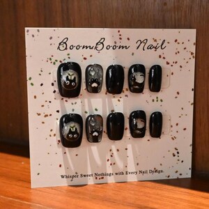 This nail set features a playful black base adorned with whimsical silver characters and patterns, adding a fun and mysterious vibe. Perfect for those who love unique, eye-catching designs with a touch of charm.