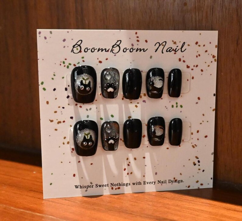 This nail set features a playful black base adorned with whimsical silver characters and patterns, adding a fun and mysterious vibe. Perfect for those who love unique, eye-catching designs with a touch of charm.