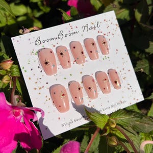This nail set features a soft nude pink base adorned with delicate golden starbursts and colorful confetti details. Perfect for a playful yet elegant look that adds a touch of sparkle to any occasion.
