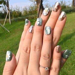 This nail set showcases a refreshing mint green base with delicate daisy accents, complemented by shimmering gold details. The design exudes a fresh and natural vibe, perfect for a cheerful and uplifting look.