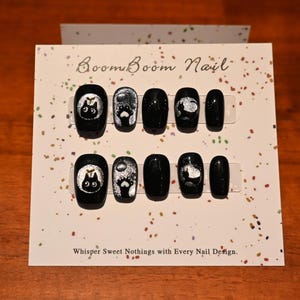 This nail set features a playful black base adorned with whimsical silver characters and patterns, adding a fun and mysterious vibe. Perfect for those who love unique, eye-catching designs with a touch of charm.