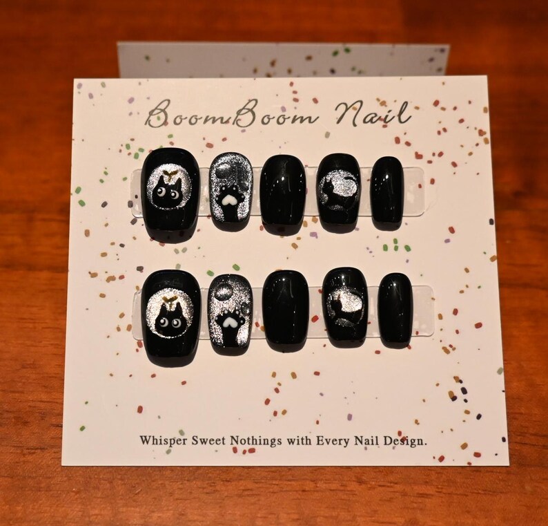 This nail set features a playful black base adorned with whimsical silver characters and patterns, adding a fun and mysterious vibe. Perfect for those who love unique, eye-catching designs with a touch of charm.