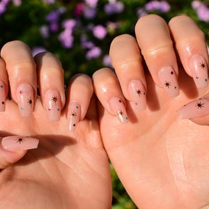 This nail set features a soft nude pink base adorned with delicate golden starbursts and colorful confetti details. Perfect for a playful yet elegant look that adds a touch of sparkle to any occasion.