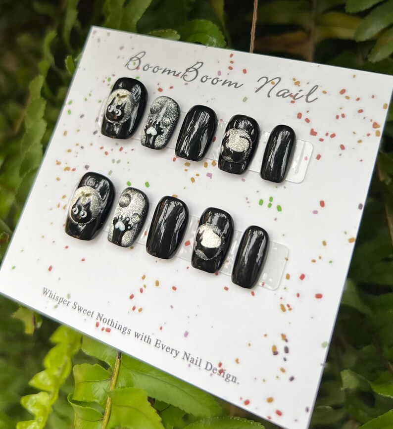 This nail set features a playful black base adorned with whimsical silver characters and patterns, adding a fun and mysterious vibe. Perfect for those who love unique, eye-catching designs with a touch of charm.