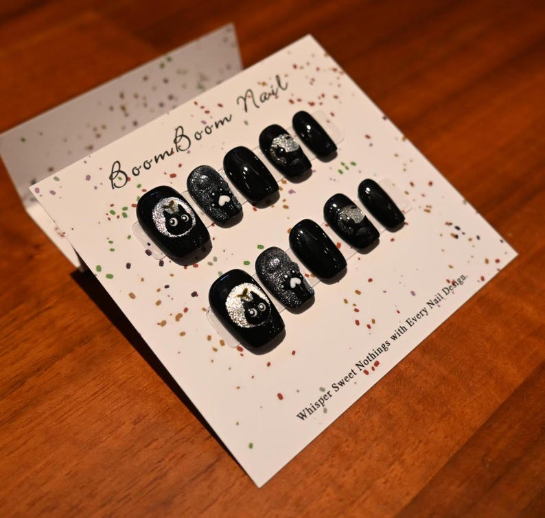This nail set features a playful black base adorned with whimsical silver characters and patterns, adding a fun and mysterious vibe. Perfect for those who love unique, eye-catching designs with a touch of charm.