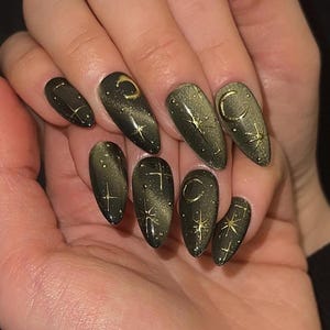 May include: Dark green almond-shaped nails with a gold cat-eye effect. Each nail features gold celestial designs, including crescent moons and stars. The nails have a glossy finish, creating a mystical and elegant look.