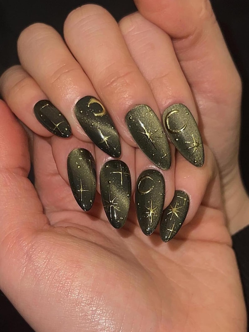 May include: Dark green almond-shaped nails with a gold cat-eye effect. Each nail features gold celestial designs, including crescent moons and stars. The nails have a glossy finish, creating a mystical and elegant look.