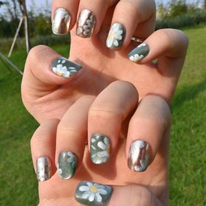 This nail set showcases a refreshing mint green base with delicate daisy accents, complemented by shimmering gold details. The design exudes a fresh and natural vibe, perfect for a cheerful and uplifting look.