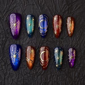 May include: A collection of ten artificial nails, each with an almond shape. The nails display colour gradients in shades like purple, blue, teal, and brown. Gold star and crescent moon patterns decorate the nails, giving a celestial appearance.