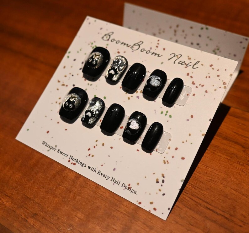 This nail set features a playful black base adorned with whimsical silver characters and patterns, adding a fun and mysterious vibe. Perfect for those who love unique, eye-catching designs with a touch of charm.