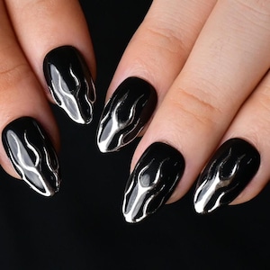 May include: Oval-shaped fingernails featuring a glossy black base coat with metallic silver flame designs painted on each nail. The silver flames are detailed with thin, reflective lines that create a high-contrast look against the dark black polish.