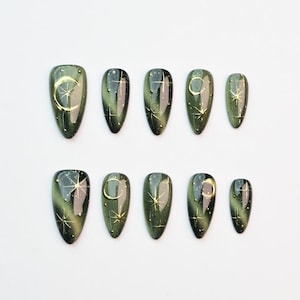 May include: Set of ten olive green press-on nails with a glossy finish. Each nail features a gold crescent moon and star design, with additional small white star accents. The nails are arranged on a white surface.