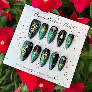 This nail set features a deep green base with intricate gold celestial designs, including stars, moons, and suns, creating a mystical and elegant look.