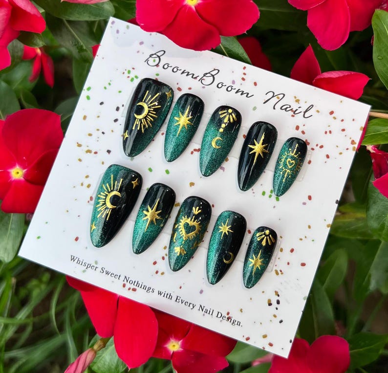This nail set features a deep green base with intricate gold celestial designs, including stars, moons, and suns, creating a mystical and elegant look.
